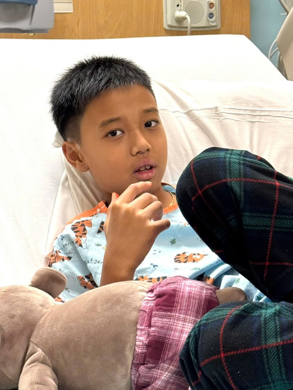 Keegan propped up in his hospital bed in a tiger-print gown.