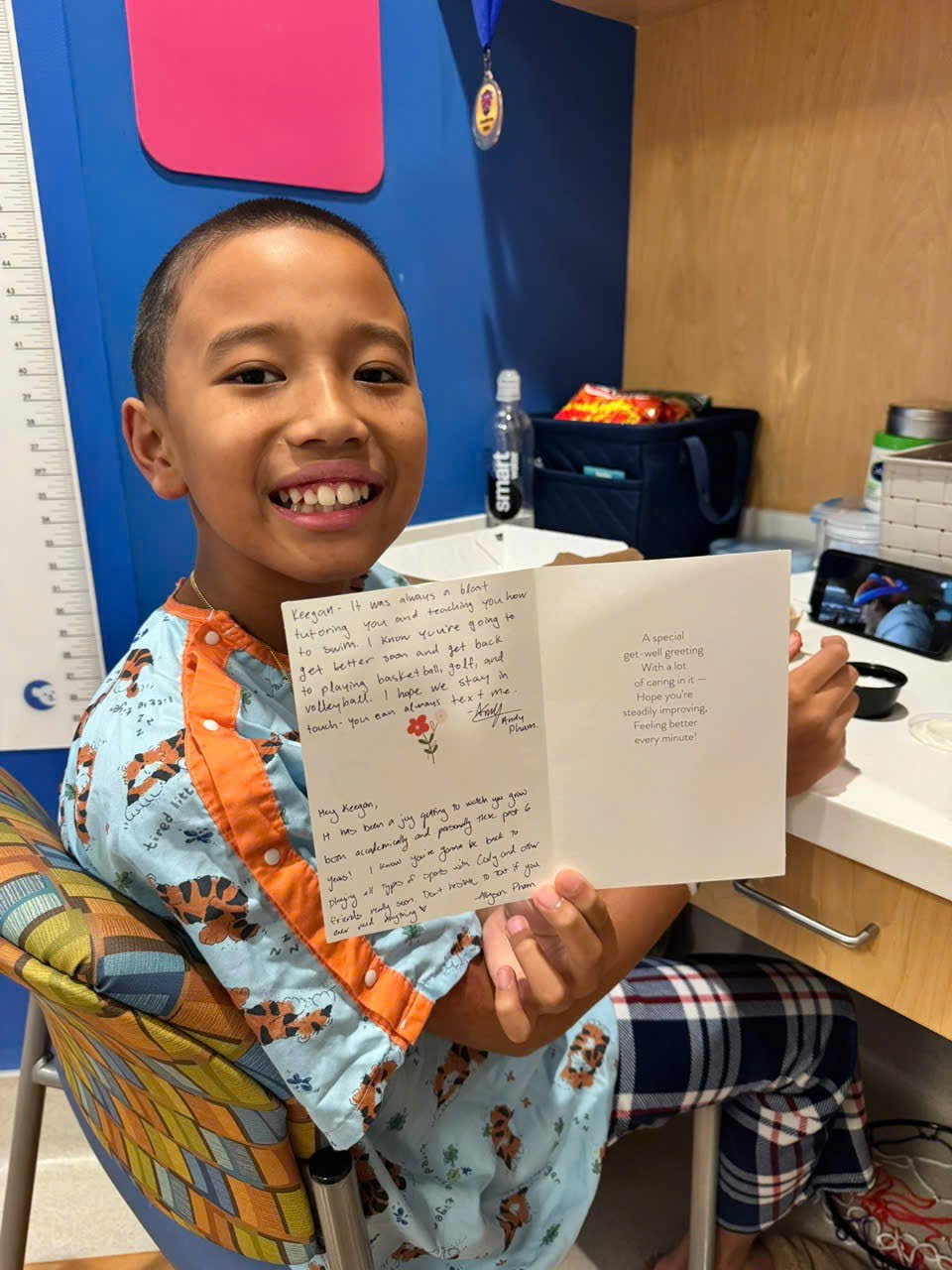 Keegan smiling widely while holding open a handwritten get-well card.