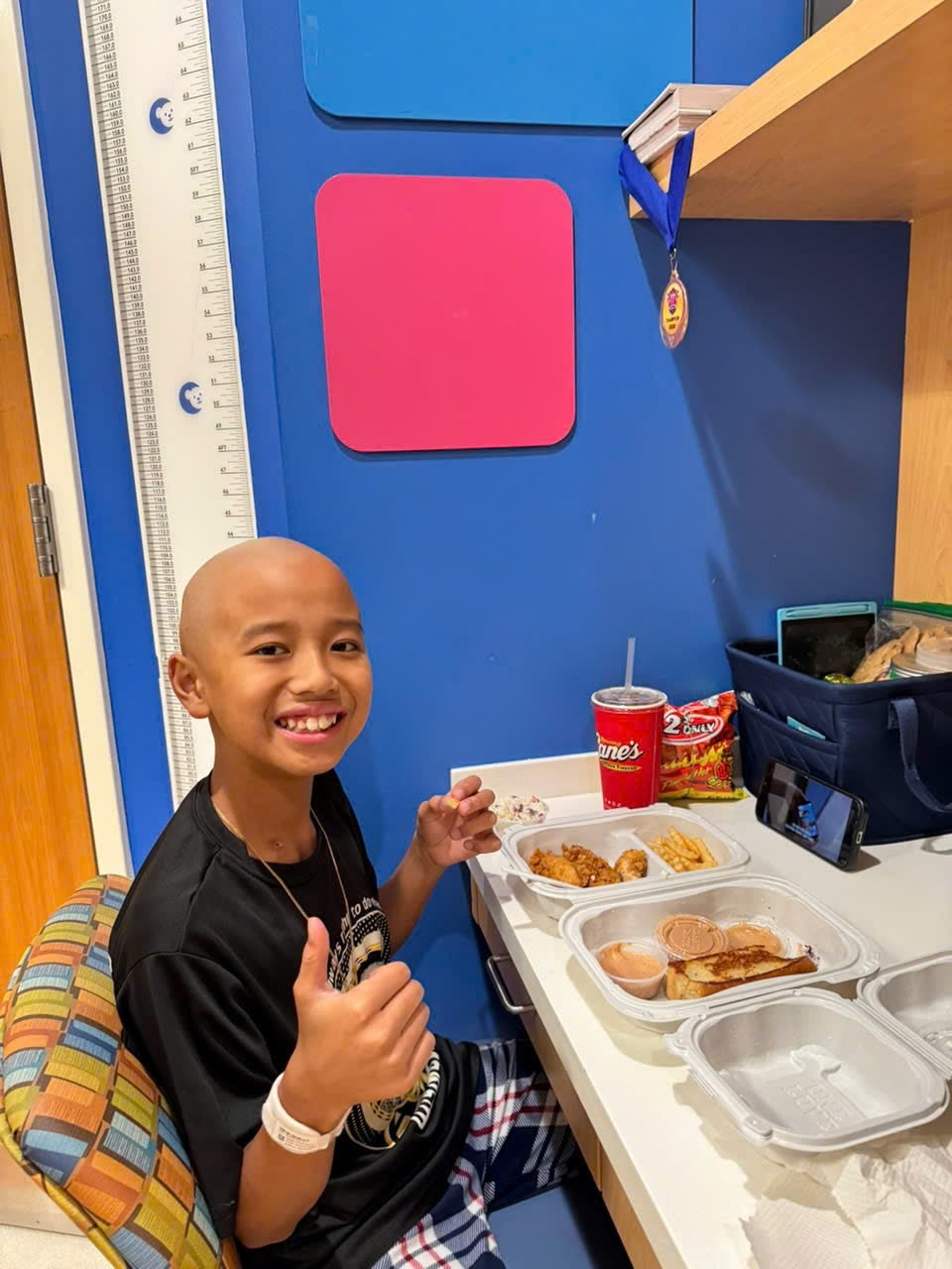 Keegan giving a thumbs up next to a takeout dinner in his hospital room.